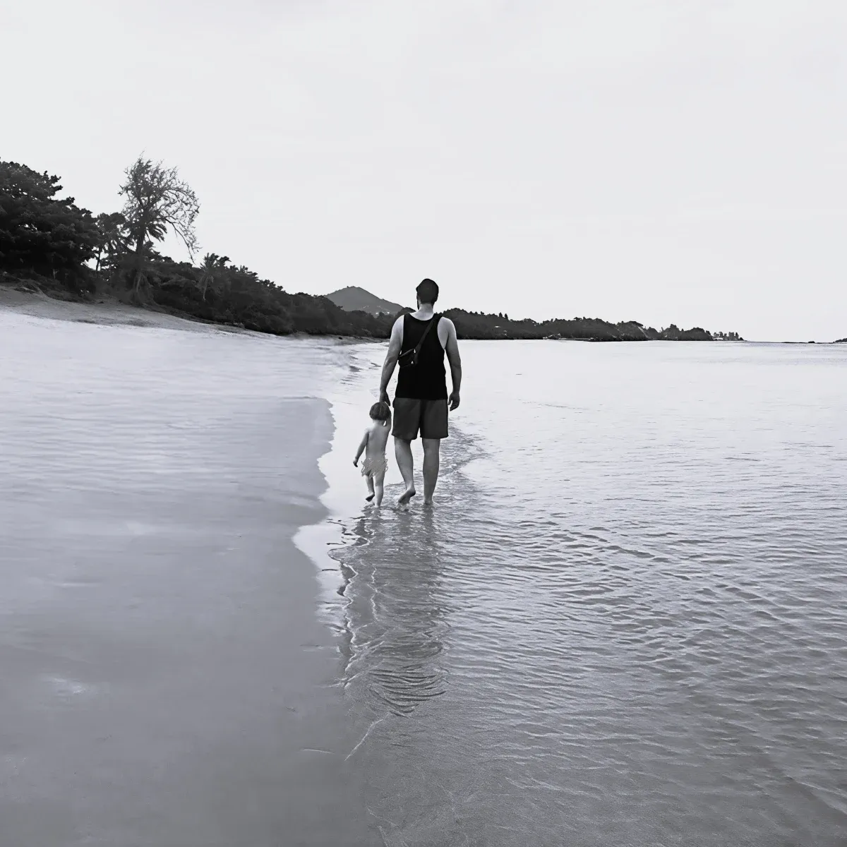 Vater und Kind gehen am Wasser den Strand entlang